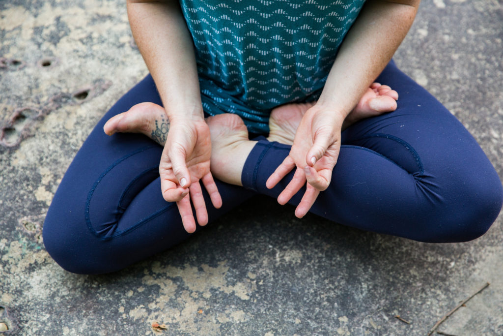 Person in a yoga pose sitting on a rock.