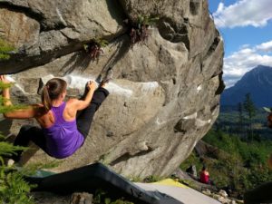 Woman climbing around the side of a boulder.