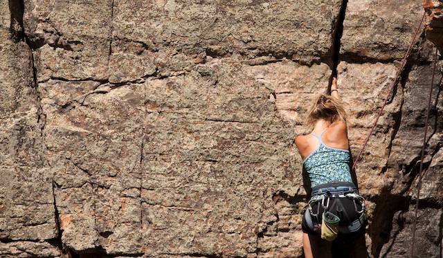 Women using crack in rock wall to assist her climb.