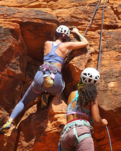 Two women rock climbing with lead belayer.