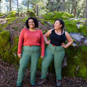 Two bigger women wearing Alpine Parrot pants and standing in the woods.