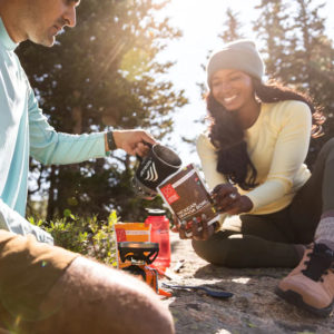 A woman holds Good to Go prepackaged food out to a man while he pours water into it.