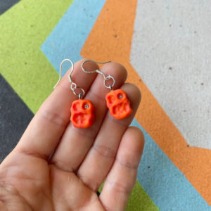 Image of hand holding small orange climbing hold earrings.